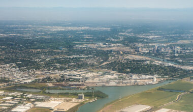 An aerial view of the city of Sacramento. High-rise buildings, a river, agricultural fields, and mountains can all be seen.