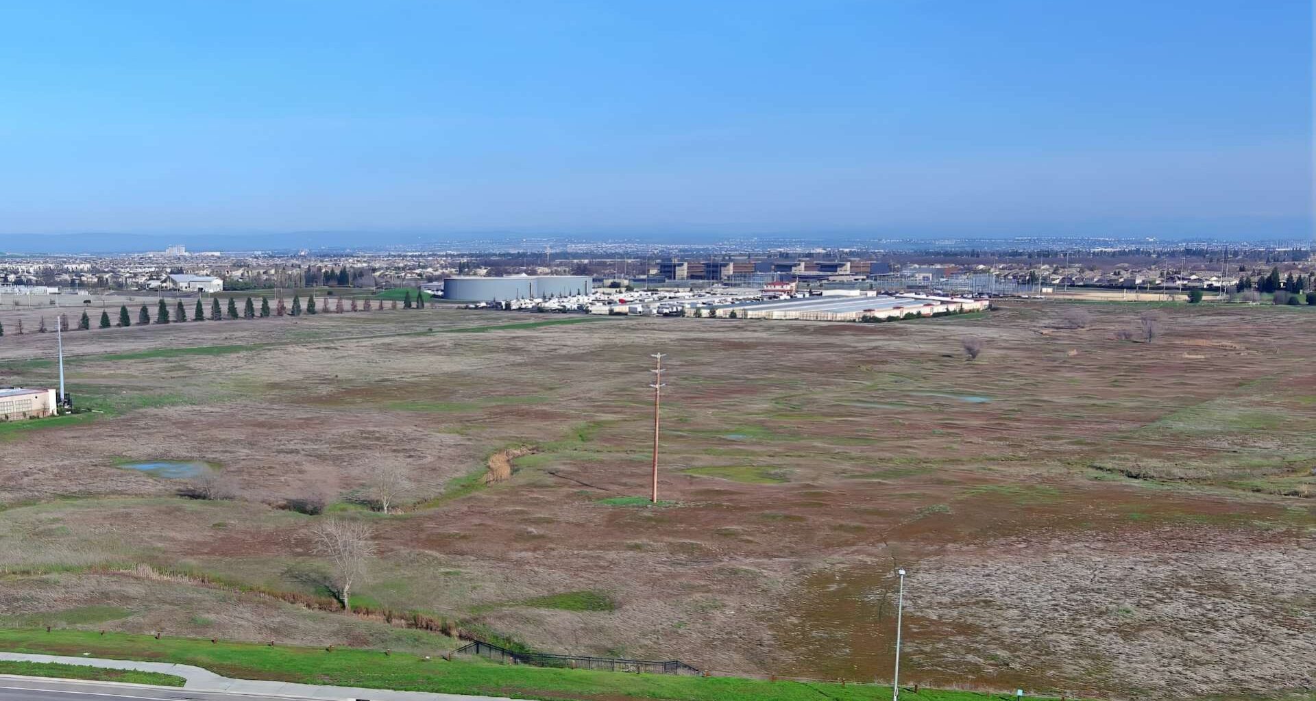 An undeveloped field near industrial buildings.