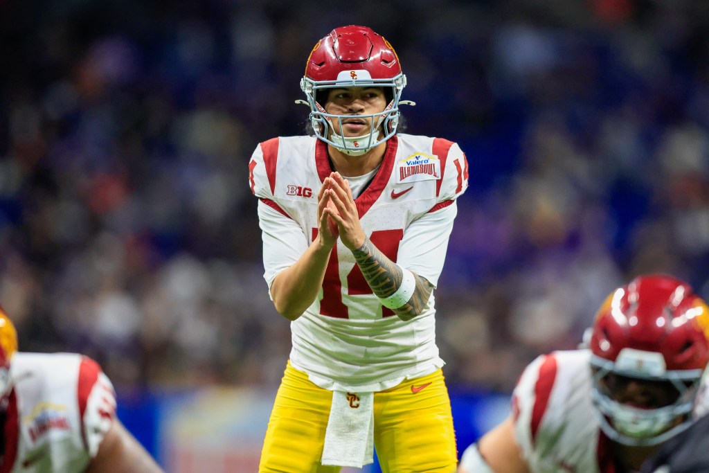 Southern California Trojans quarterback Jayden Maiava, wearing a red helmet and a white jersey with "BIG" and "Valero Alamo Bowl" patches, stands on the field with his hands clasped in front of him.