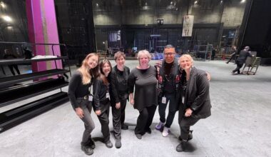 Six production team members pose together backstage in a theater.