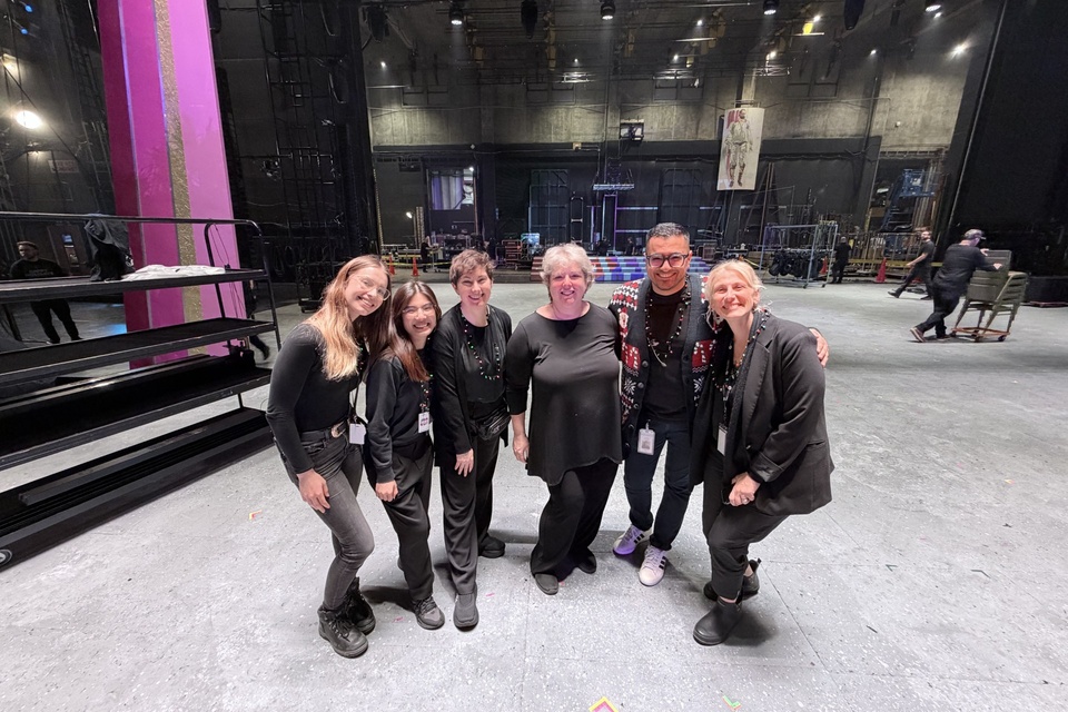 Six production team members pose together backstage in a theater.