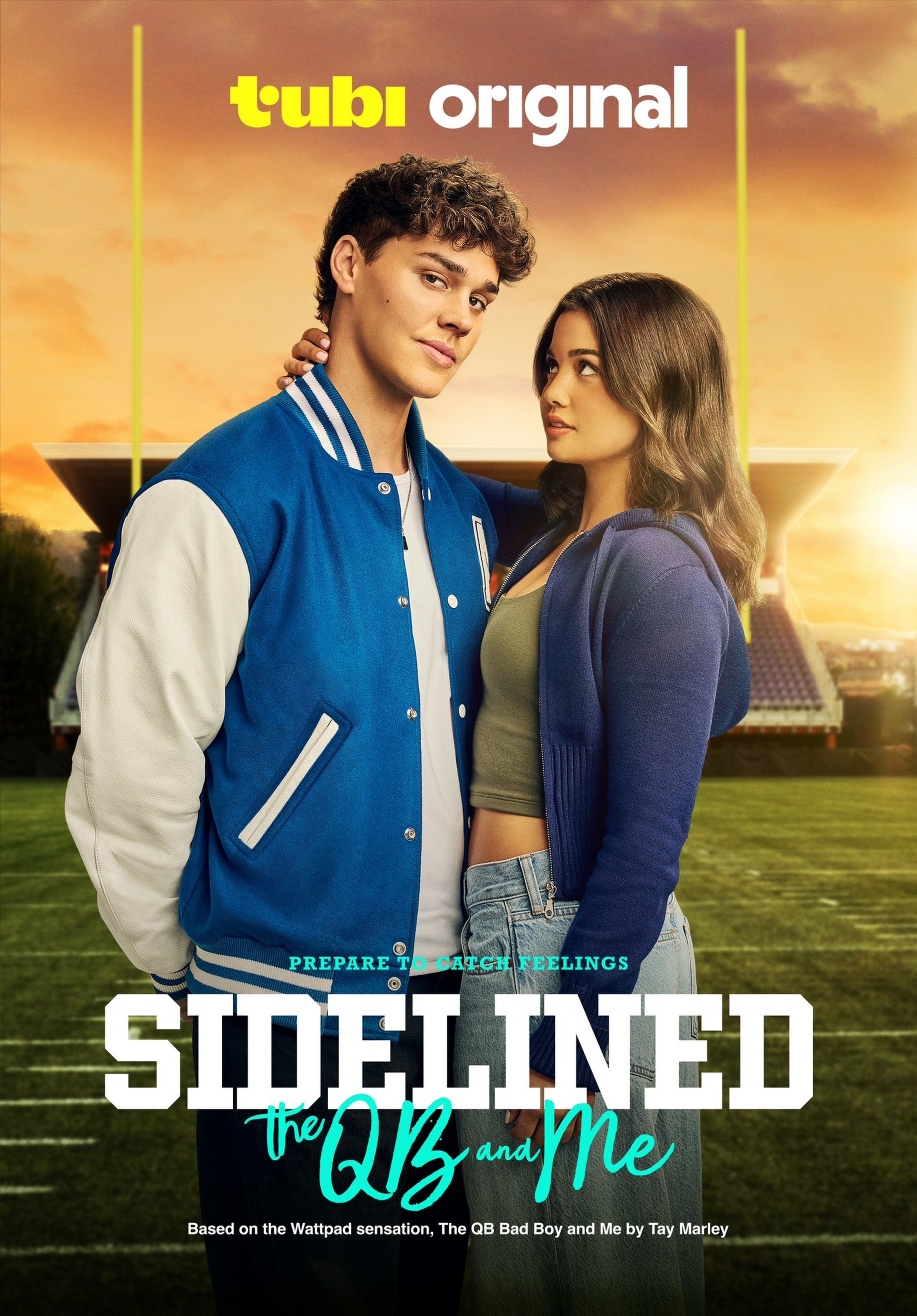 A young man in a blue letterman jacket stands with his arm around a young woman in a purple hoodie on a football field at sunset.