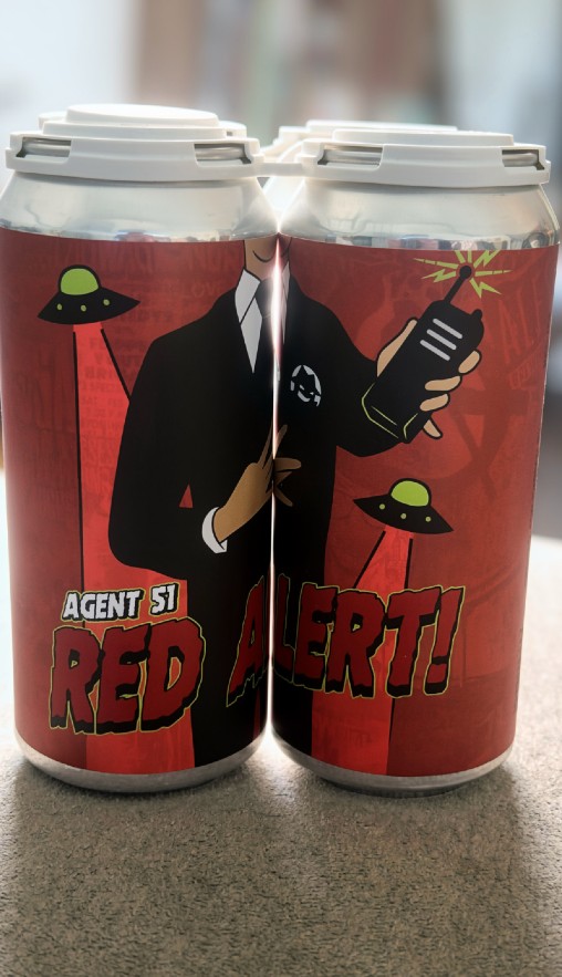 Two beer cans side by side, each fitting together to display an image of a man in a black suit with a radio in hand and flying saucer hovering behind him.