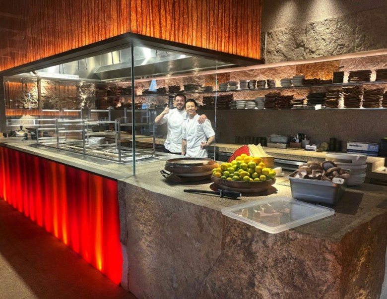 Two men embrace and smile in a large professional open kitchen.