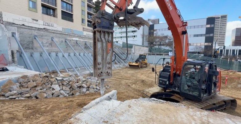A large construction site, with machinery and amid dirt and a large cracked slab, which is due to become affordable housing.