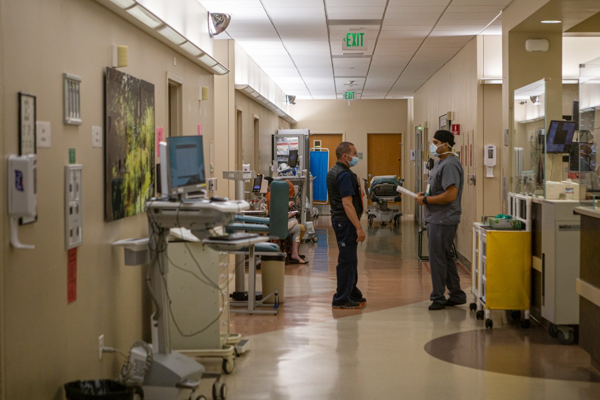 Two medical professionals wearing masks and medical scrubs hold paperwork in a hospital hallway.