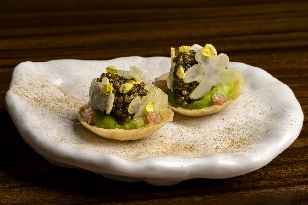 Two gourmet appetizers with caviar, avocado, and edible flowers on a decorative plate.
