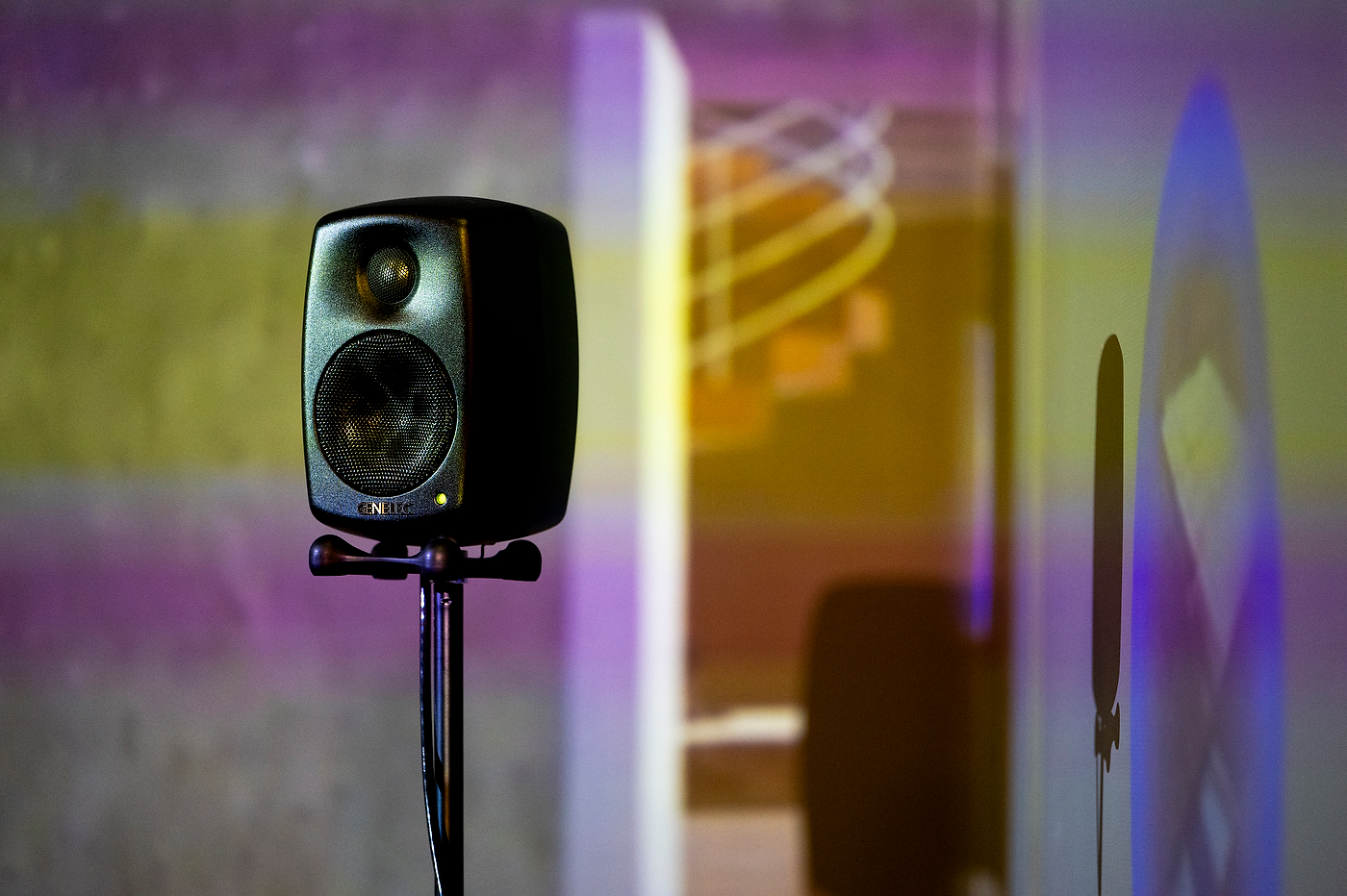 A studio speaker on a stand, backlit by colored projection light.