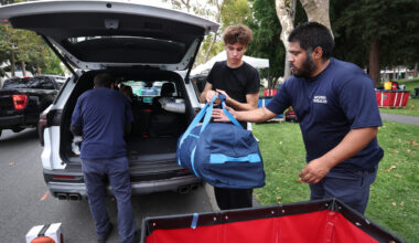 Two Northeastern move-in staff help a student unload a duffel bag from an SUV's open trunk.