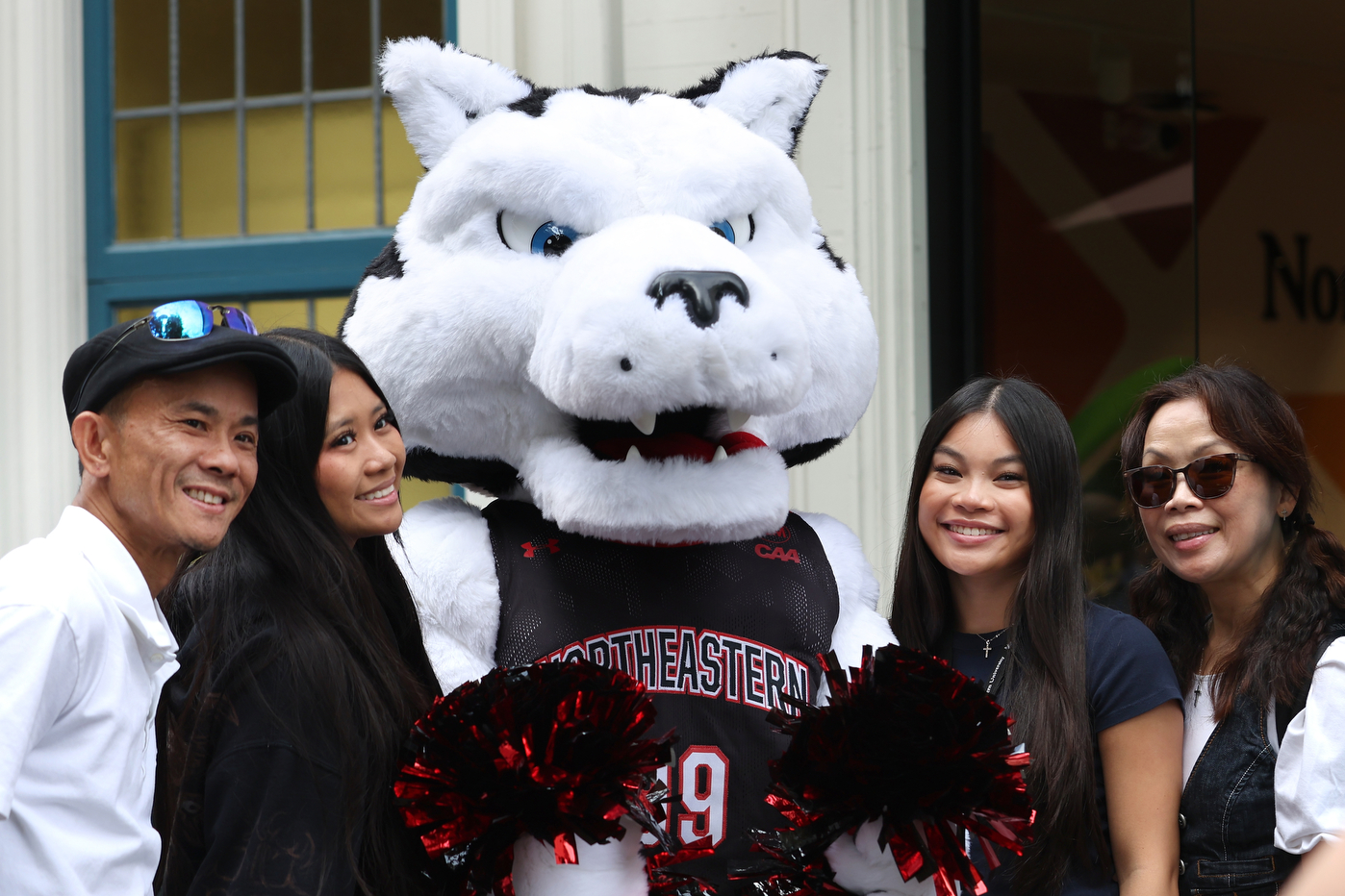 A family poses with Northeastern's husky mascot outside a campus building during move-in day.