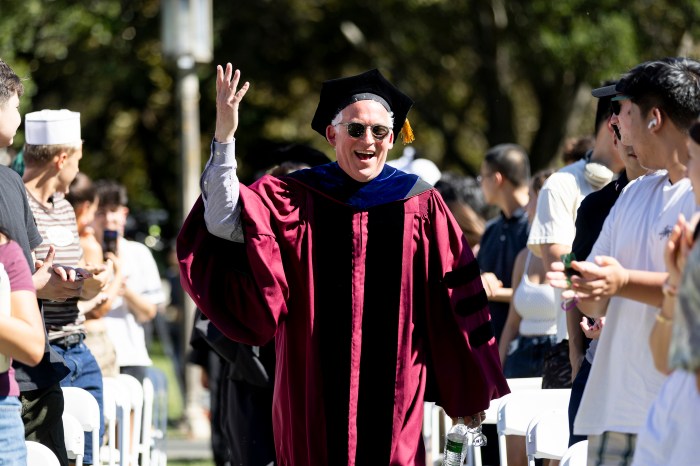 Daniel Sachs waving to the crowd while wearing academic regalia, smiling.