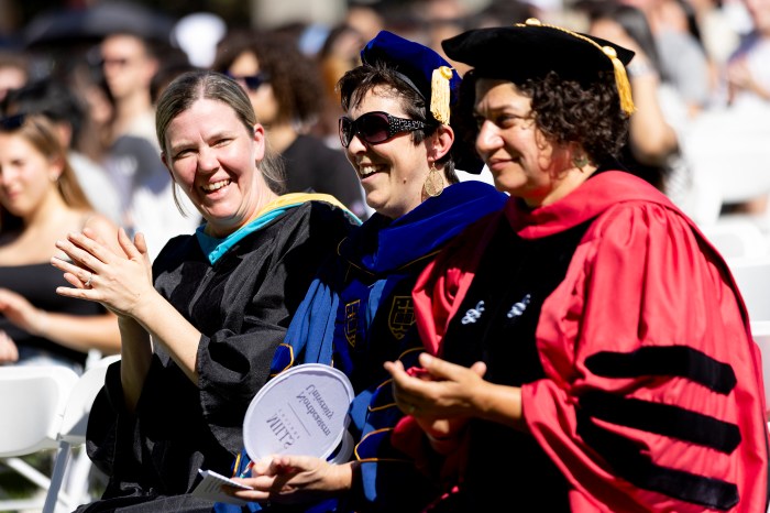Three faculty members in academic regalia laughing and applauding together.