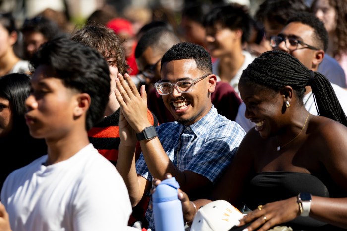 Students smiling and clapping in a crowd.