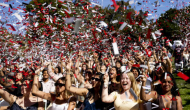 Students cheering with arms raised as red, white, and black confetti fills the air above the crowd.
