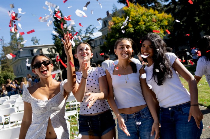 Four students laughing as confetti falls around them.