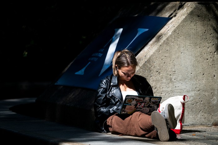 A student works on a laptop beside a Northeastern University banner and stone pillar.