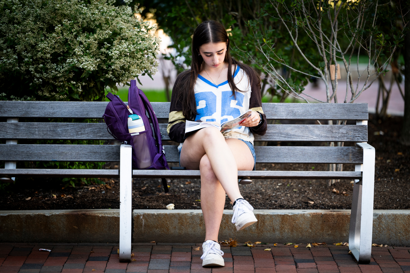A student reads a magazine while sitting on a bench in Krentzman Quad, with a backpack beside her.