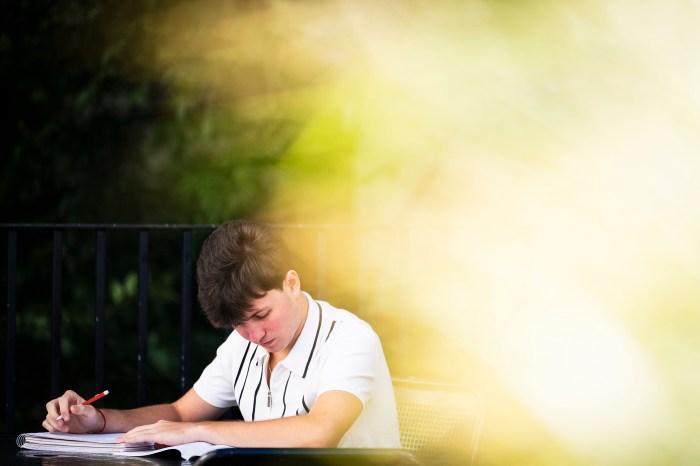 A Northeastern community member writes in a notebook outside Hayden Hall, with sunlight filtering through foliage.