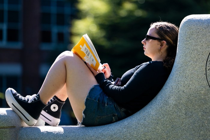 Grace Biondo reclines on a stone bench, reading a book in Centennial Common.