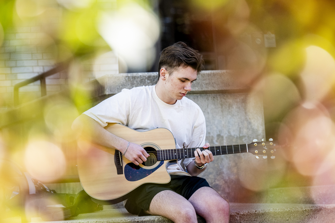 Jack Bottamini, a business administration student, plays guitar while seated outdoors at Krentzman Quad.