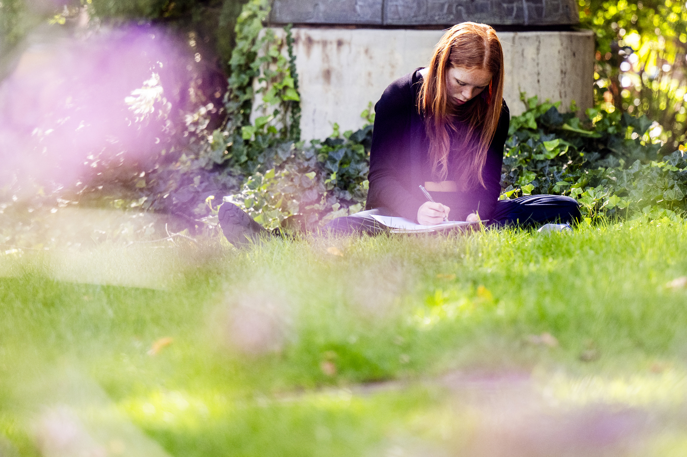 A student writes in a notebook while sitting on the grass outside Curry Student Center.