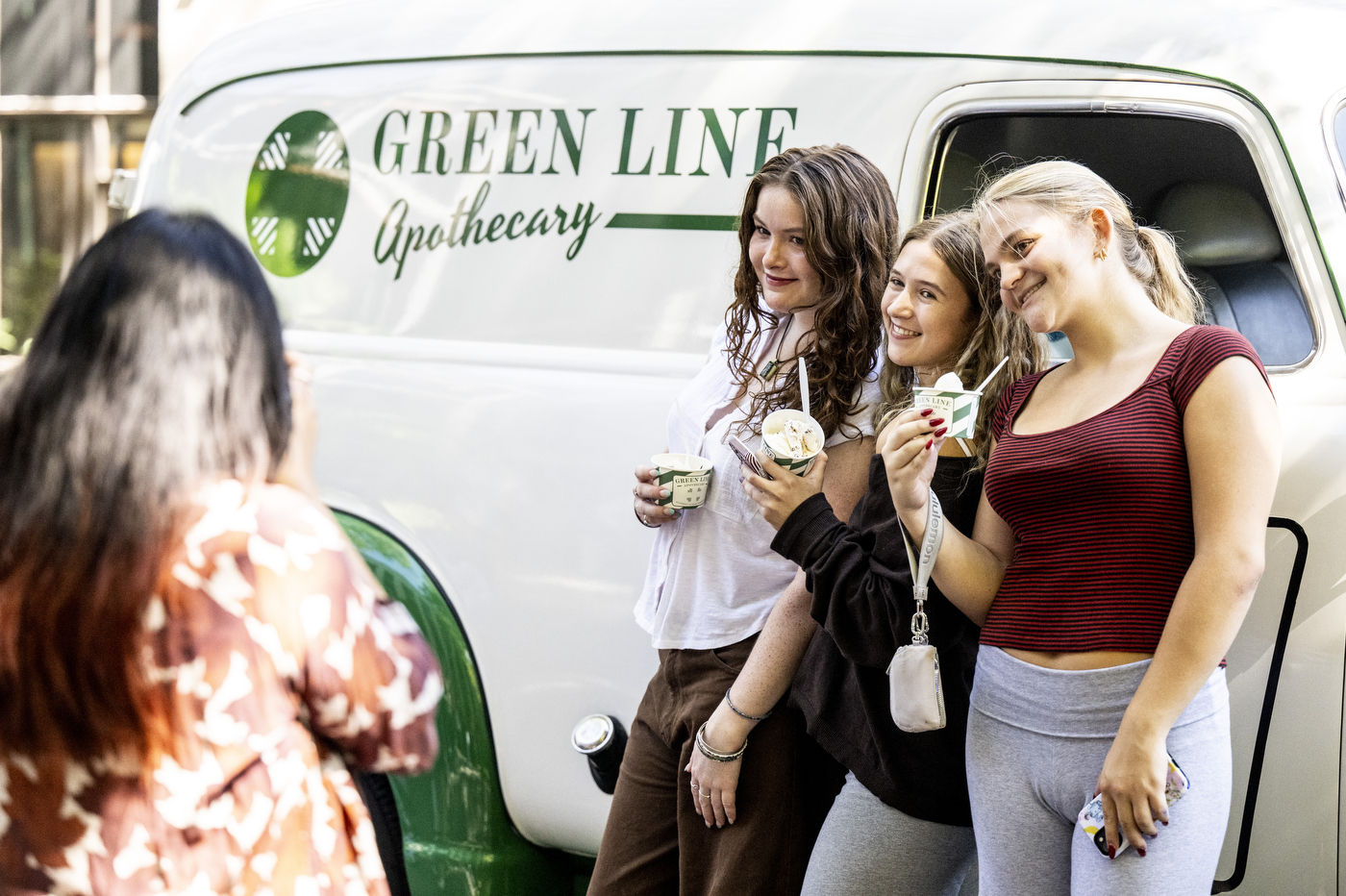 Three students hold cups of ice cream while standing in front of the Green Line Apothecary truck.