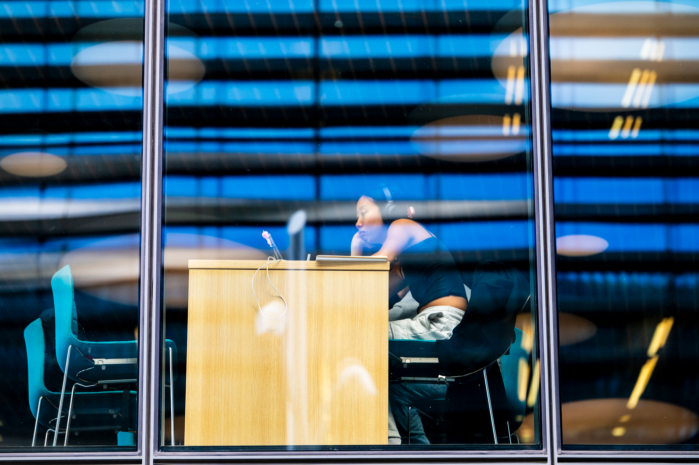 A student studies at a podium inside ISEC, viewed through window blinds from outside.