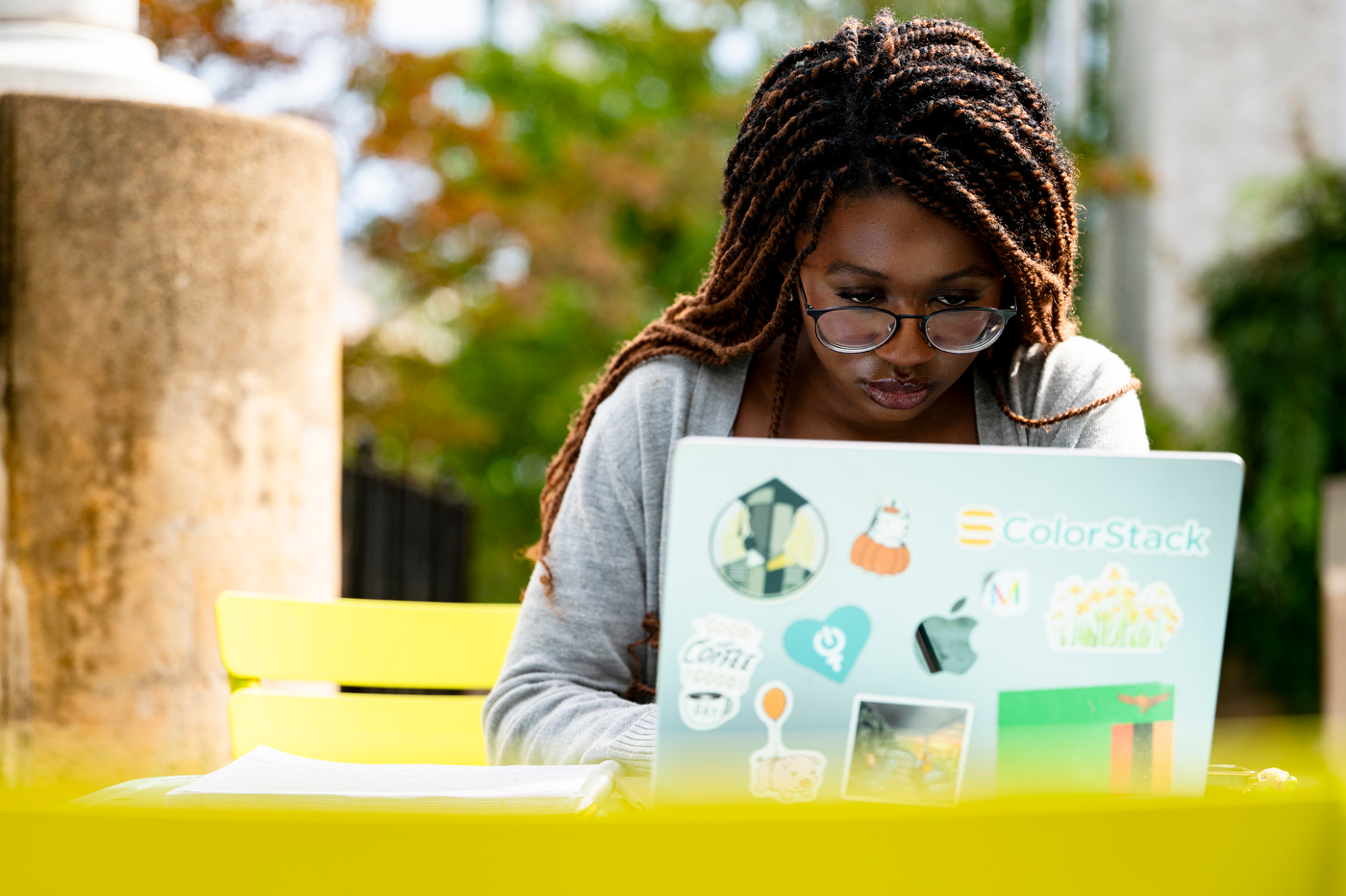 A student wearing glasses looks at a laptop covered in stickers, including one for ColorStack.