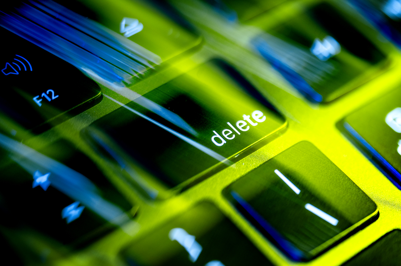 A robotic hand hovers over a keyboard's delete key, lit in green and blue tones.
