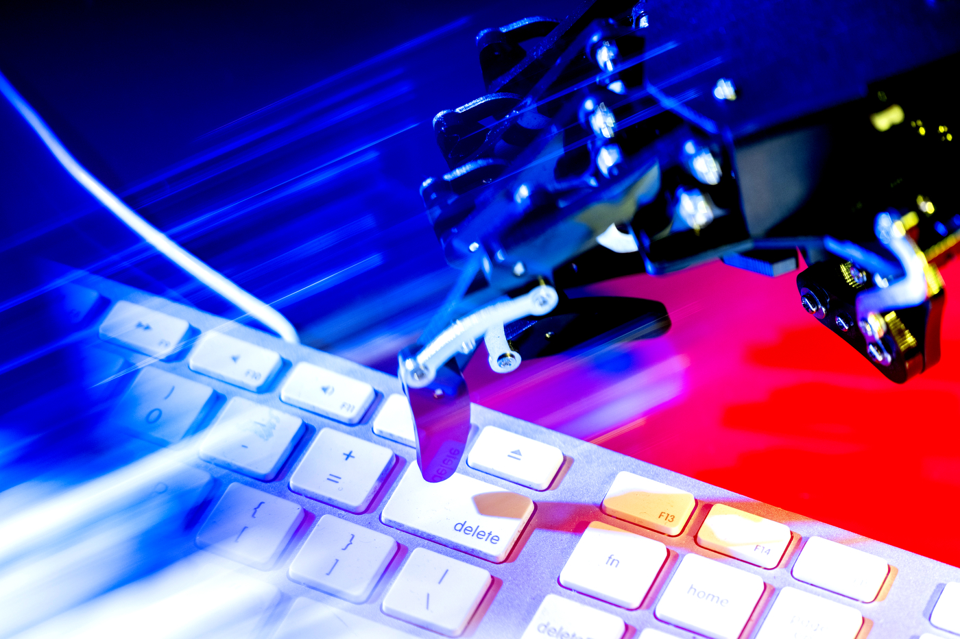 A robotic hand reaches toward a keyboard, illuminated in dramatic blue and red lighting.