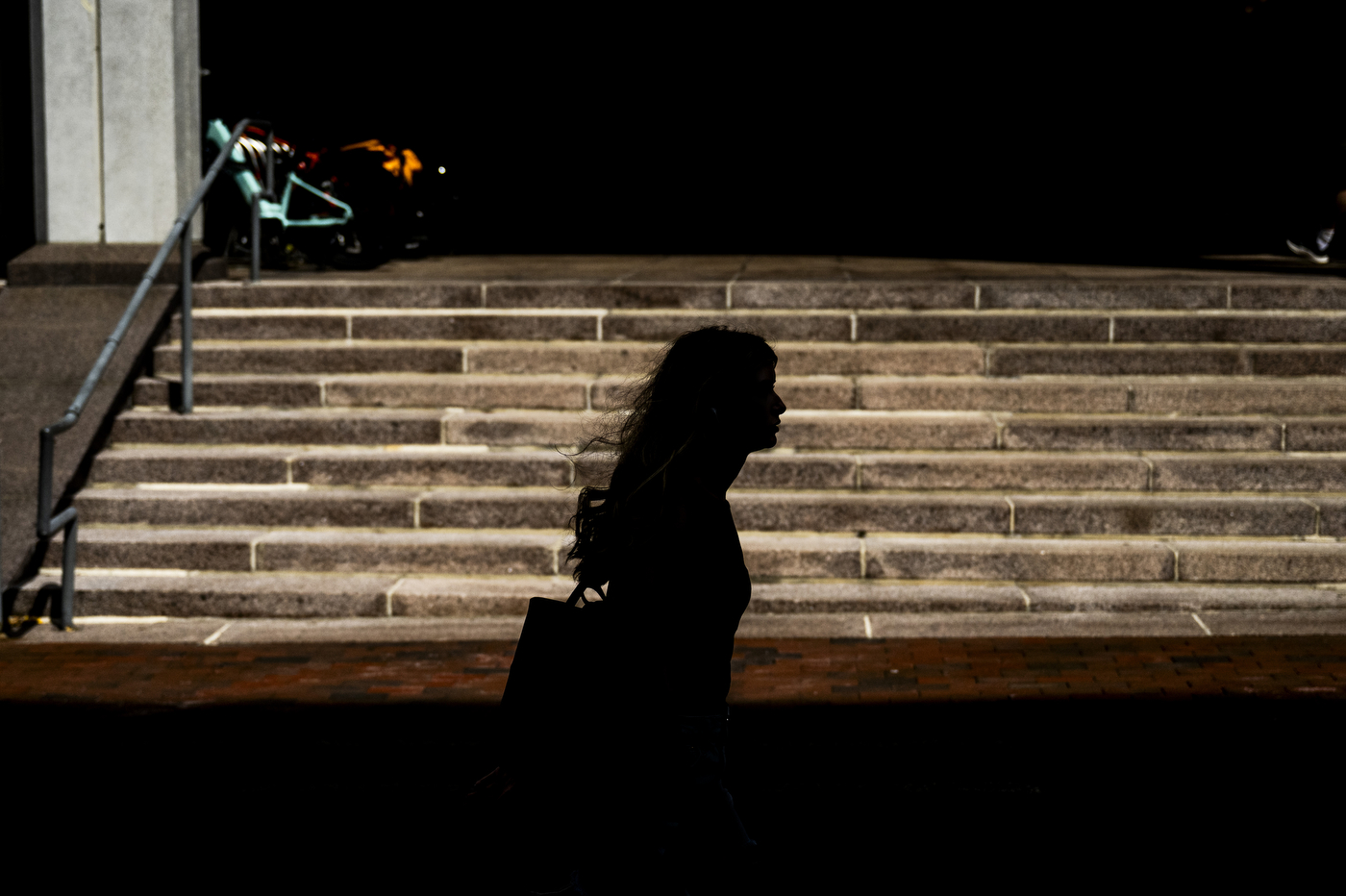 A student's silhouette is visible walking up outdoor stairs near Snell Library at night.