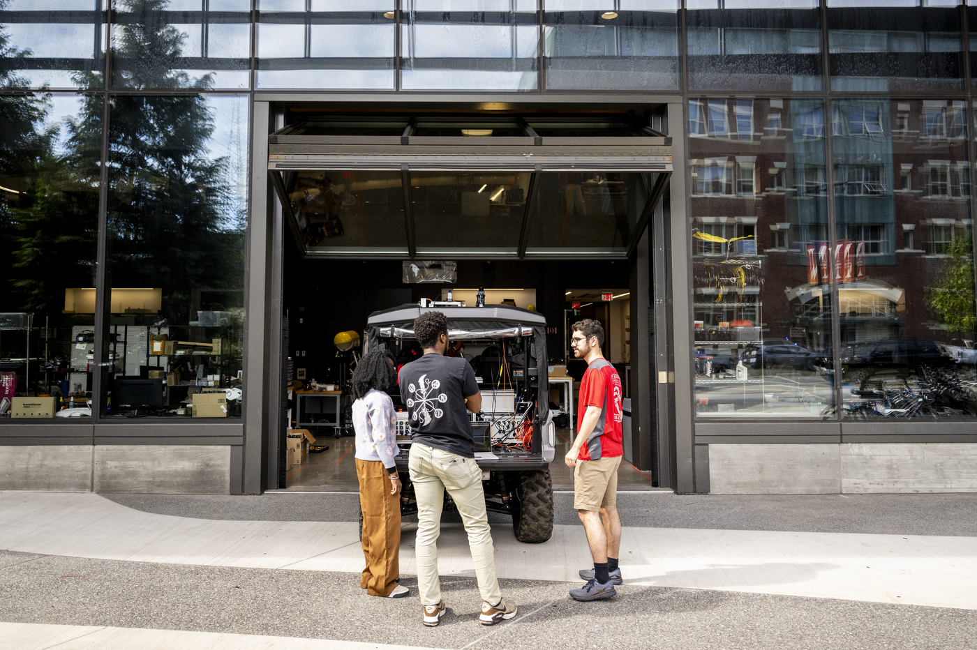 Aidan Reichenberg, James Tukpah, and Wisena Joseph work on an autonomous vehicle outside the EXP building's entrance.