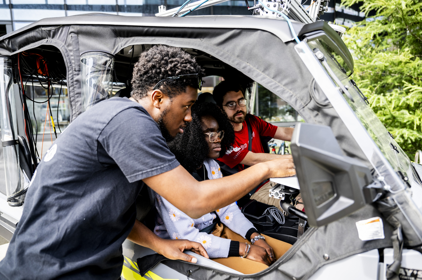 Aidan Reichenberg, James Tukpah, and Wisena Joseph examine a control panel inside an autonomous all-terrain vehicle.