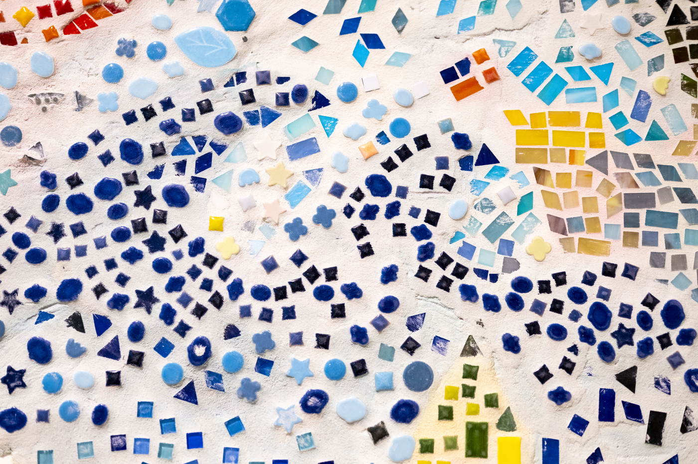 Close-up detail of a mosaic artwork with blue, yellow, and white tiles forming an abstract pattern.