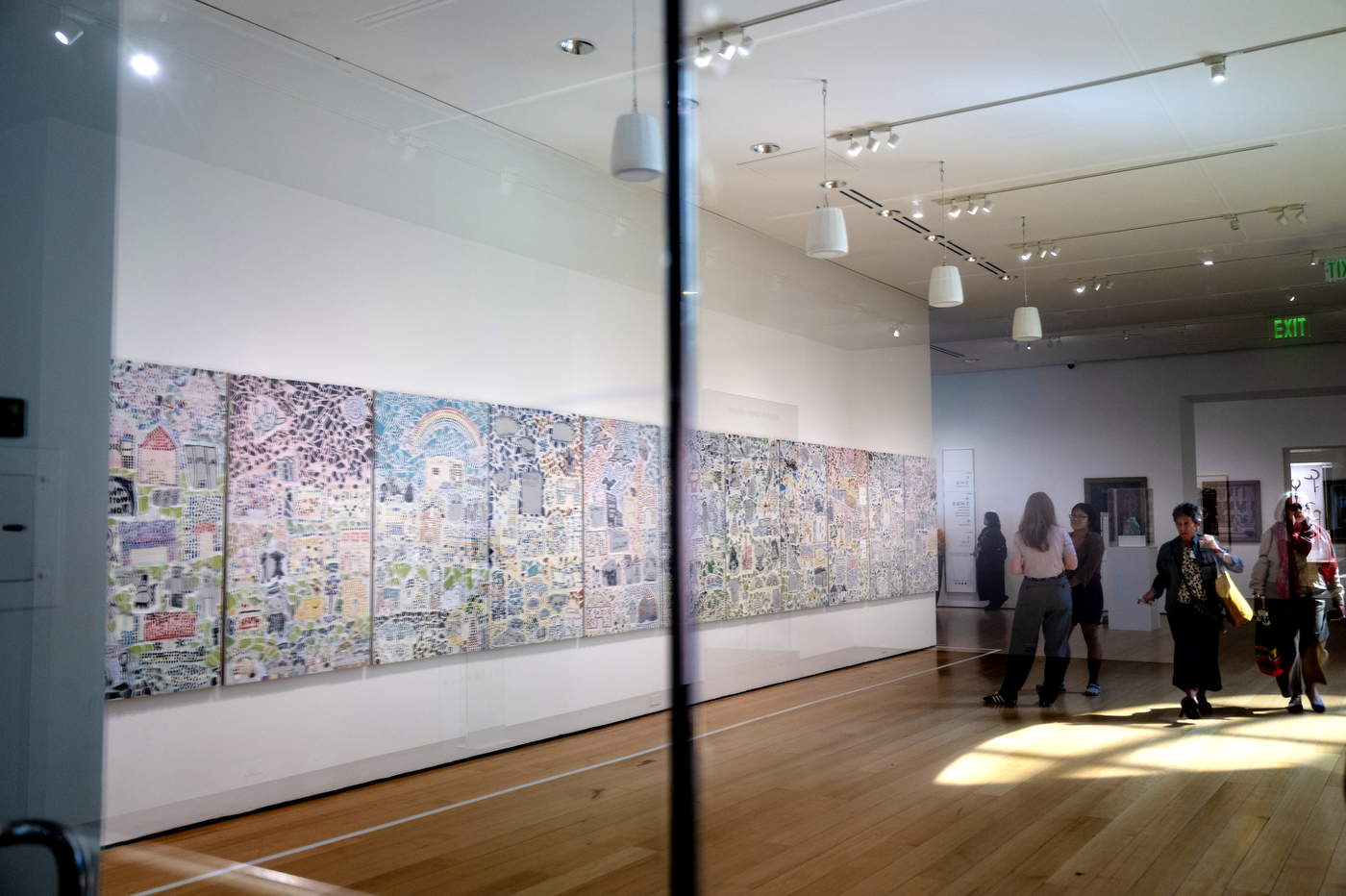 Museum visitors view a row of mosaic art panels displayed along a gallery wall.