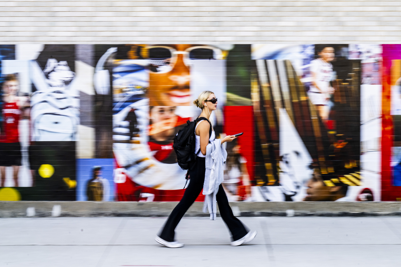 A student walks past a colorful mural with a blurry background effect.