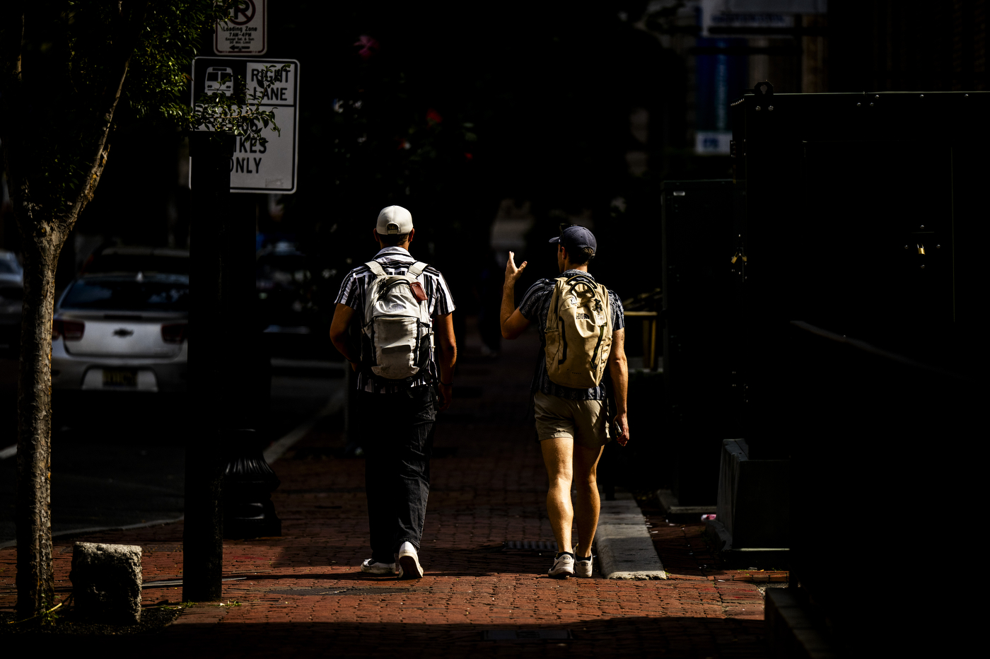 Two students walk along a city street near campus, backlit in silhouette.