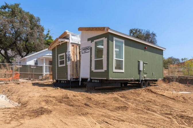 A modular house appears to be split in two. It rests on a dirt lot.