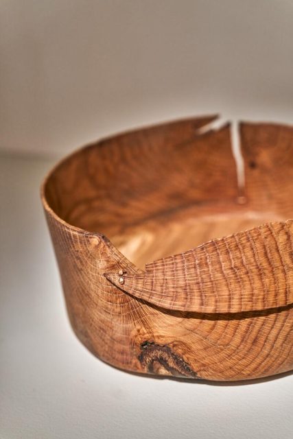 A wooden bowl with a visible natural grain, featuring a repaired crack secured with metal staples or rivets.
