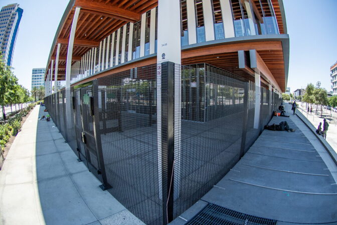 A metal fence surrounds a building as some people sit and lay outside of it.