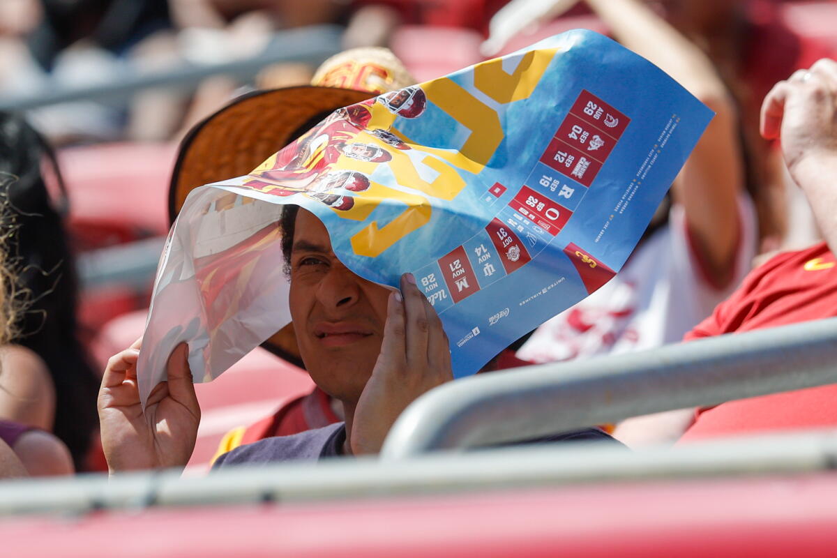 A fan covers takes cover under a poster during USC's season opener against San José State Saturday at the Coliseum.