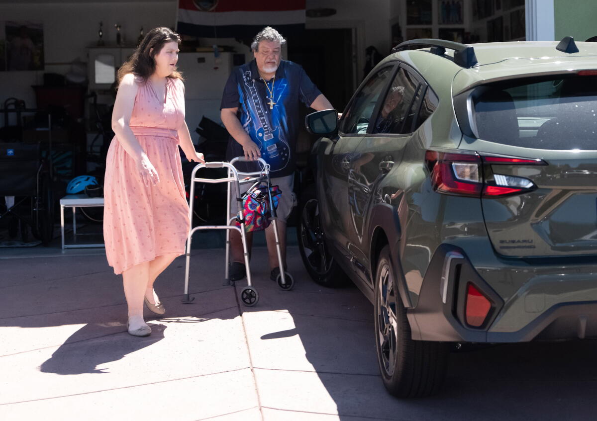 Sarah Lawlor helps Rudy Ramirez with his walker next to a parked vehicle