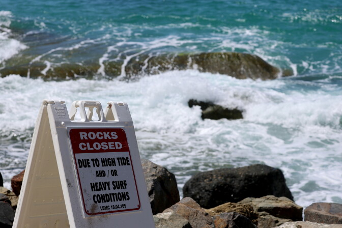 A rocks closed sign is posted in a beach near rocks.