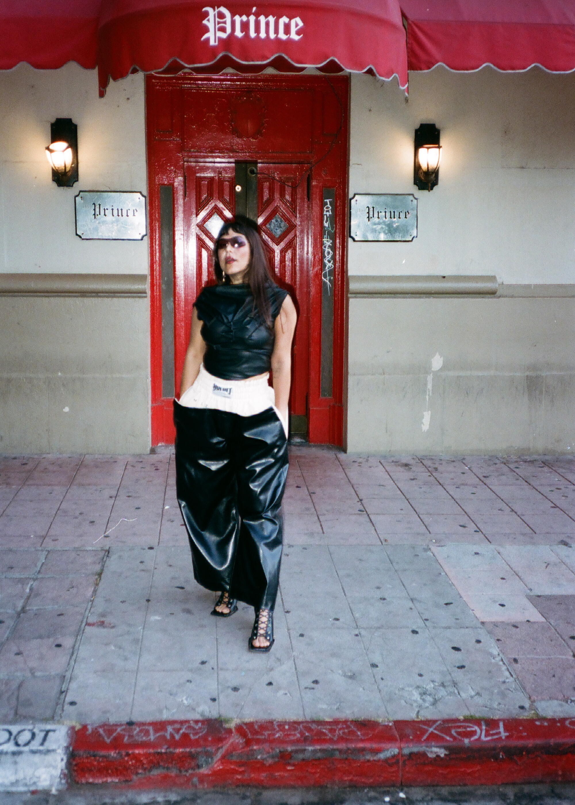 Holcomb in front of the Prince. Styled by Jocelyn Corona, wearing AYANEGUI, TANAMACHI and Vacr.