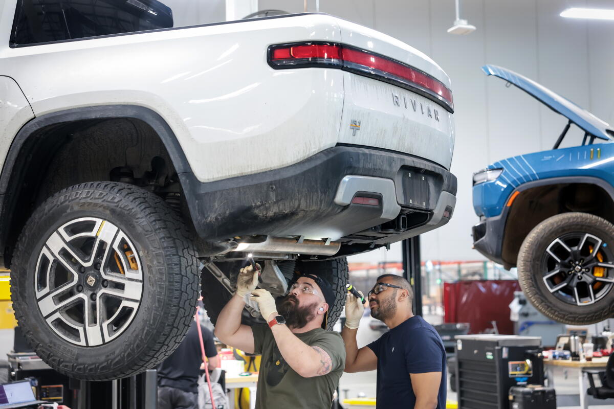 Two men working on an elevated white vehicle in a facility