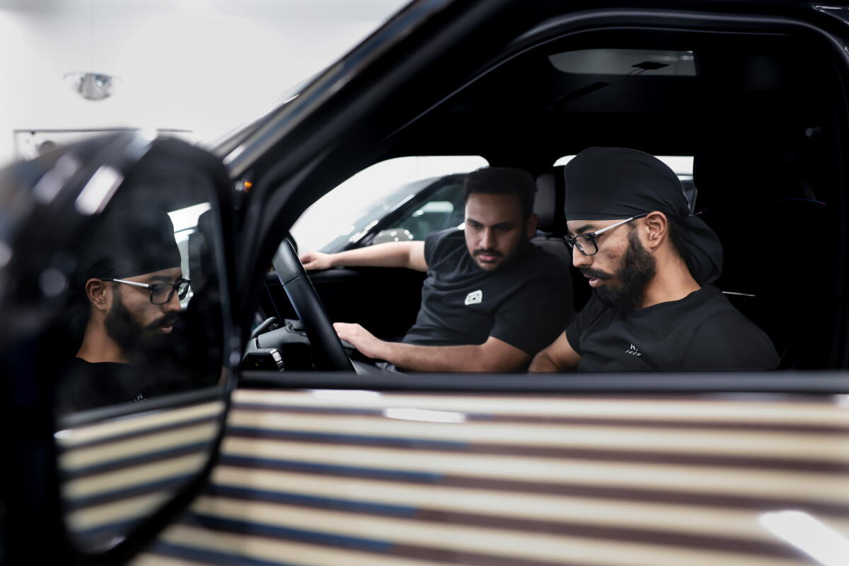 Two men seated at the front of a car, looking down at the controls