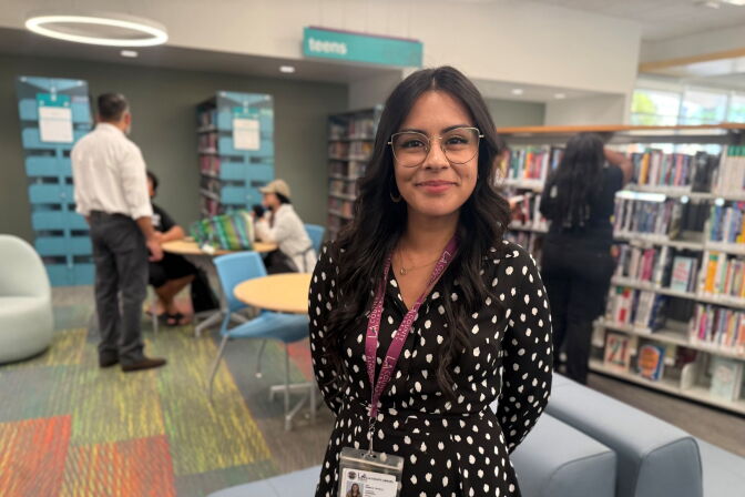 A woman with medium-light skin tone and glasses poses for a picture in a library.