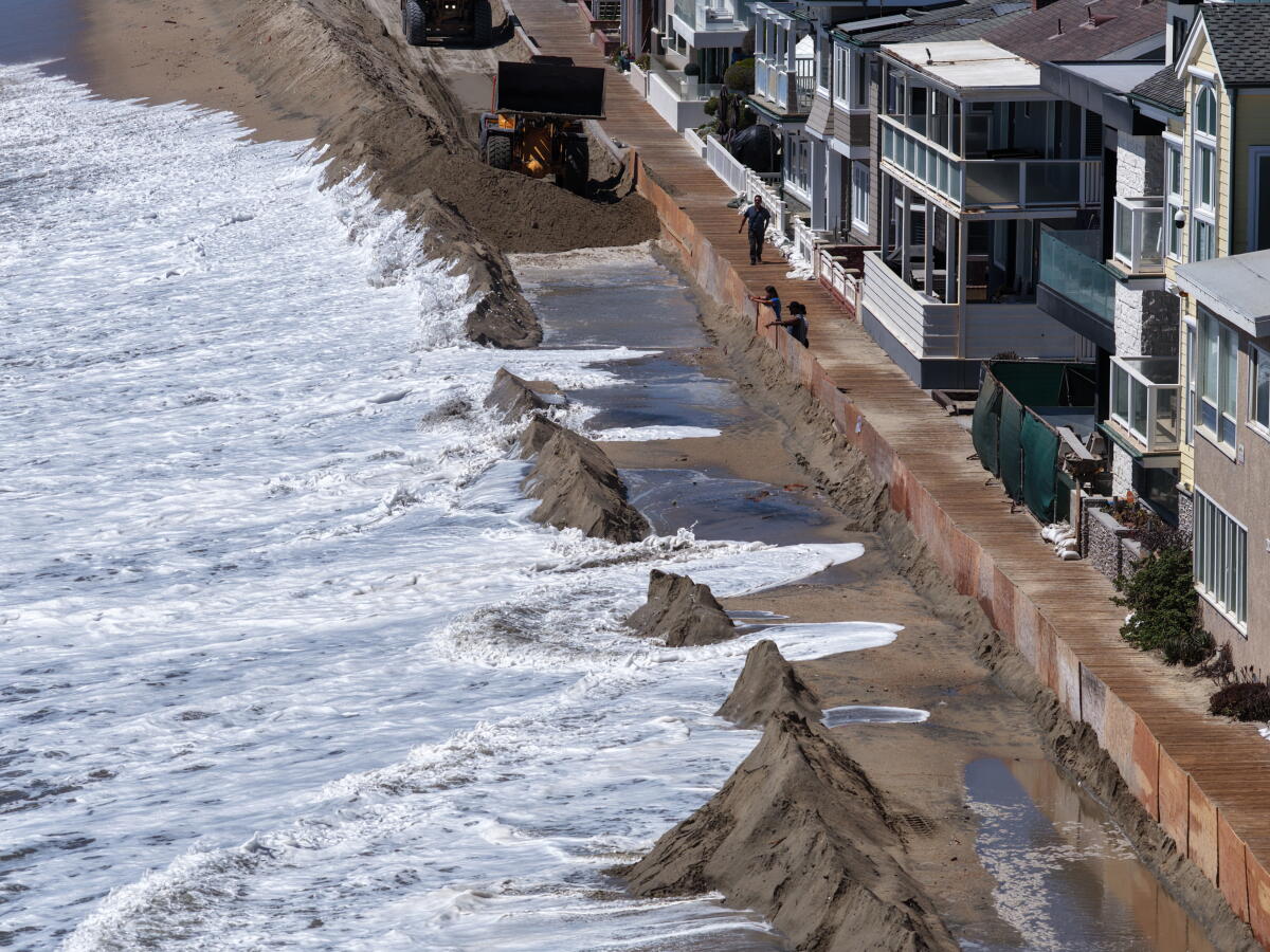 Bystanders watch as water rushes over a sand berm and maintenance crews rush to fortify the berms.