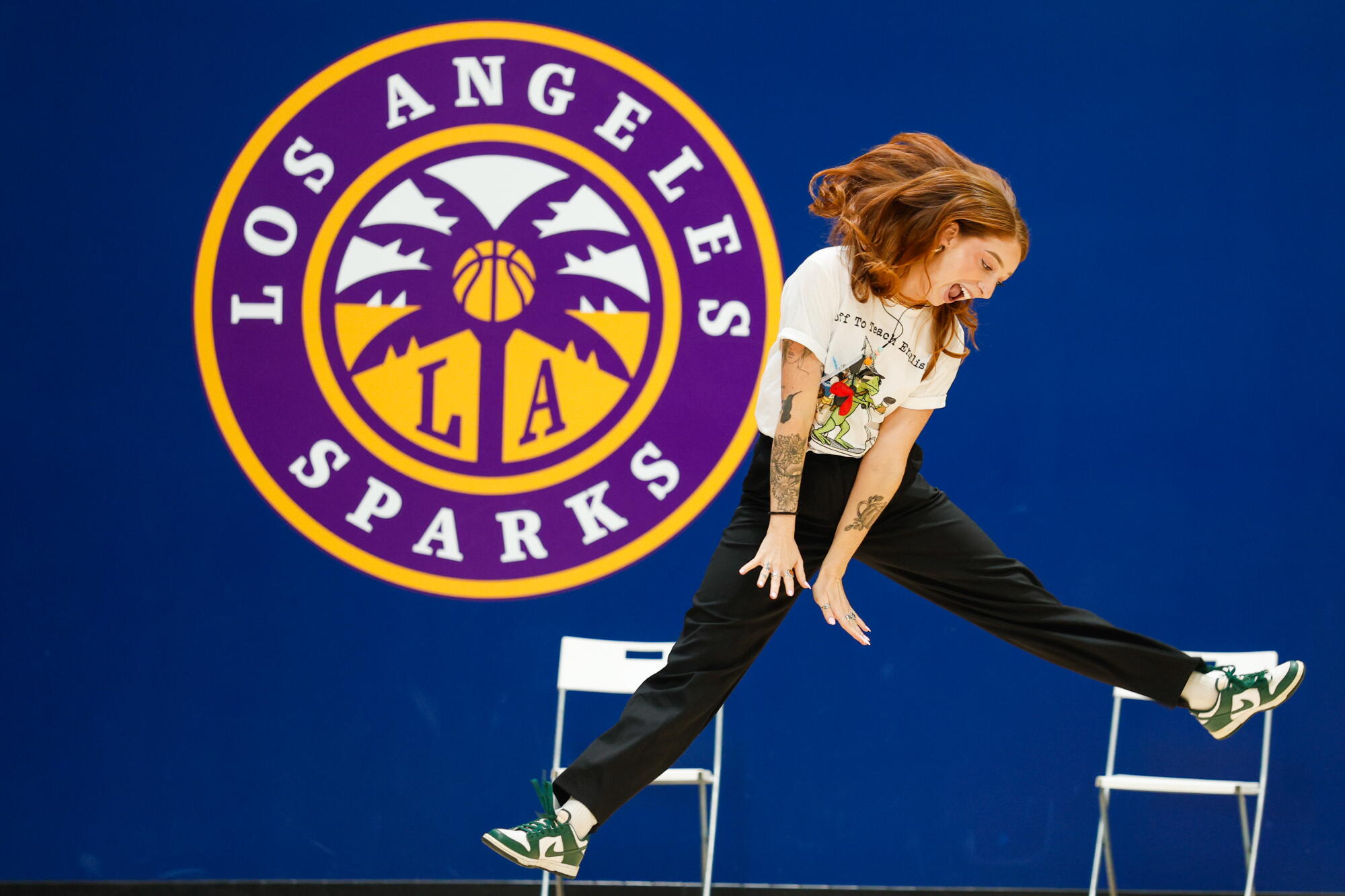 a teacher leaps in the air in front of her school's logo