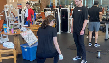 A kinesiology student guides an employee through an exercise routine in the gym.